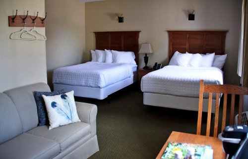 A cozy hotel room featuring two beds, a sofa, a wooden chair, and a small table with a magazine.