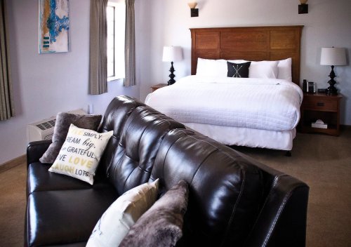 Cozy hotel room featuring a king bed, a leather sofa, and decorative pillows, with natural light from a window.