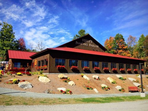 A charming pancake parlor with a red roof, surrounded by colorful flowers and trees under a blue sky.