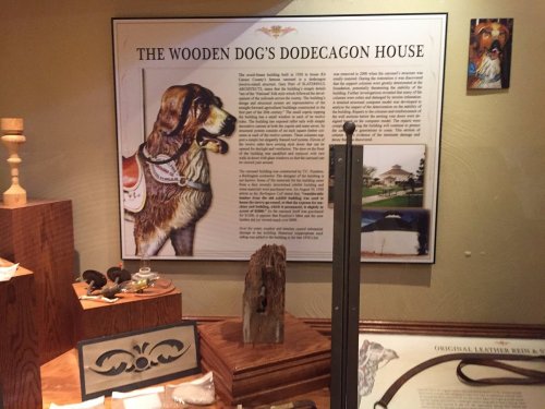Exhibit display featuring "The Wooden Dog's Dodecagon House" with a dog portrait and various artifacts on wooden surfaces.