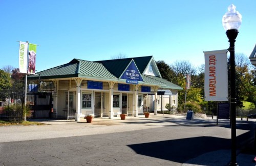 Entrance of the Maryland Zoo, featuring a green roof, banners, and a clear blue sky.