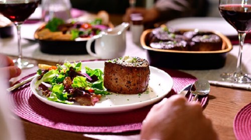 A beautifully plated meal featuring a steak and a fresh salad, with wine glasses in the background.
