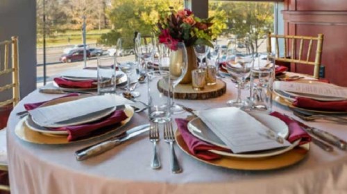 Elegant dining table set with gold and red accents, featuring plates, glasses, and a floral centerpiece.