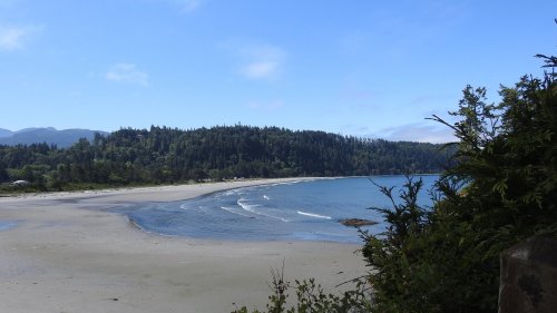 A serene beach scene with gentle waves, surrounded by lush green hills under a clear blue sky.