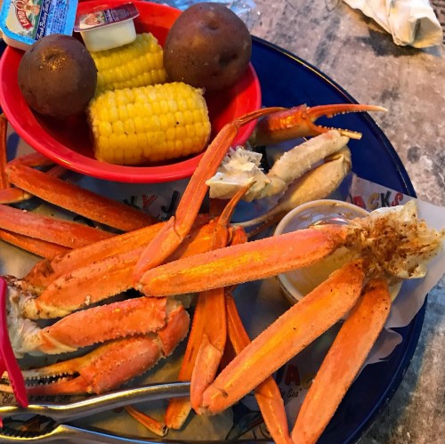 A blue plate with crab legs, corn on the cob, two potatoes, and a small cup of dipping sauce.