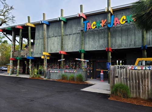 Colorful exterior of Tacky Jack's restaurant with wooden pillars and vibrant signage, surrounded by greenery.