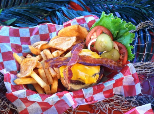 A delicious cheeseburger topped with bacon, lettuce, tomato, and pickles, served with fries and potato chips in a basket.