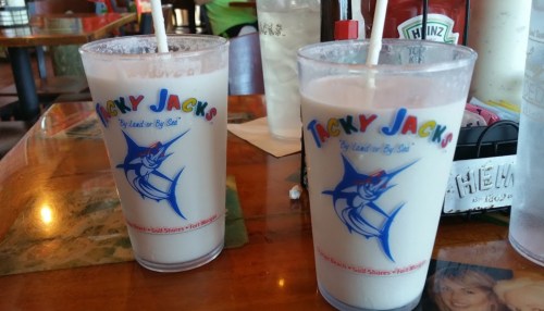 Two frosty drinks in Tacky Jack's branded cups on a wooden table, with a straw in each.