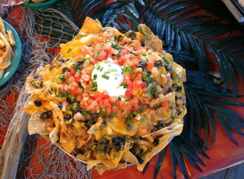 A colorful plate of nachos topped with cheese, black beans, diced tomatoes, green onions, and a dollop of sour cream.