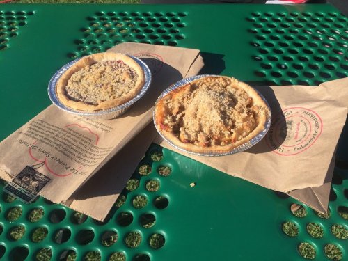 Two pies on a green table, one with a crumb topping and the other with a nutty topping, resting on brown paper.
