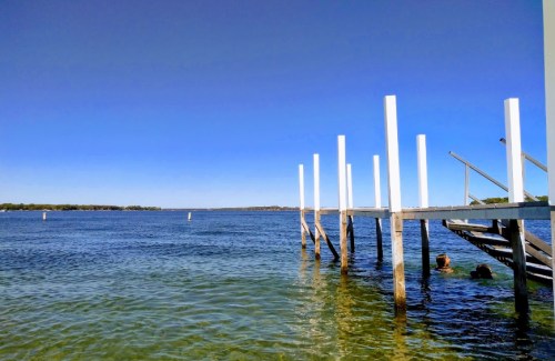 A serene waterfront scene featuring a wooden dock extending into calm water under a clear blue sky.