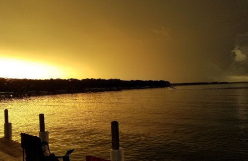 A serene lake at sunset, with golden hues reflecting on the water and dark clouds in the distance.