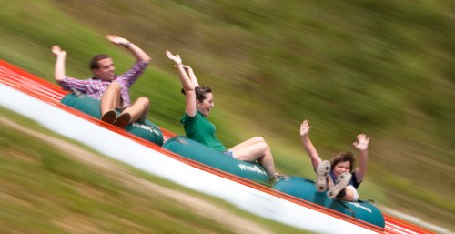Three people joyfully sliding down a hill on inflatable tubes, arms raised in excitement.