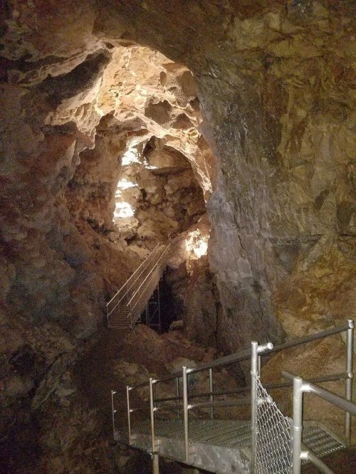A dimly lit cave with rocky walls and a metal walkway leading deeper into the cavern.