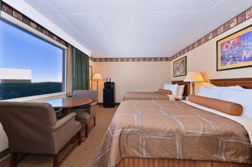 A hotel room with two beds, a table, chairs, and a window, featuring warm decor and soft lighting.