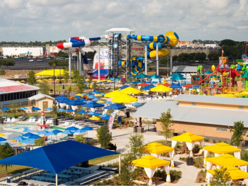 A vibrant water park scene with colorful slides, umbrellas, and attractions under a blue sky.