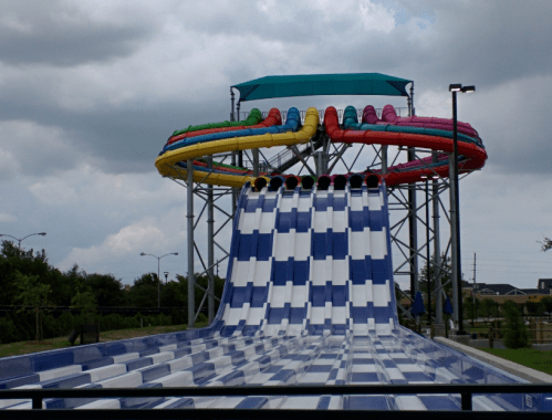 A colorful water slide with multiple loops and a steep drop, set against a cloudy sky.