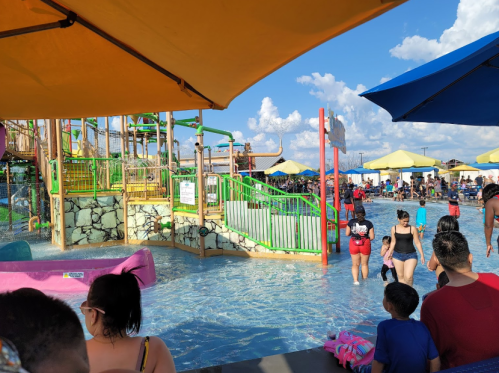 A vibrant water park scene with colorful slides, people enjoying the water, and umbrellas providing shade.