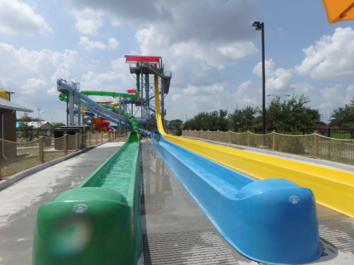Colorful water slides in a sunny water park, featuring green, red, yellow, and blue slides with a clear blue sky.
