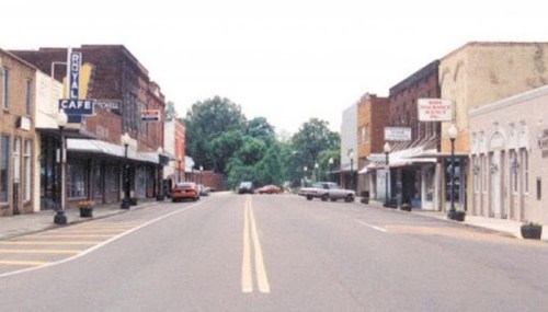 A quiet main street lined with shops and cafes, featuring vintage buildings and a few parked cars.
