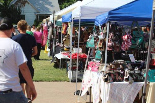 A bustling outdoor market with colorful tents displaying various handmade goods and accessories. People are browsing.