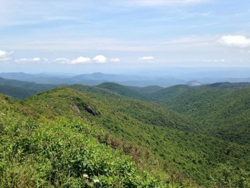 Lush green mountains stretch into the distance under a clear blue sky, with soft clouds scattered above.