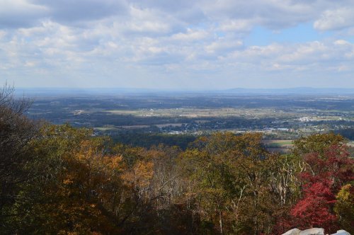 A panoramic view of a valley with colorful autumn foliage and a cloudy sky in the background.
