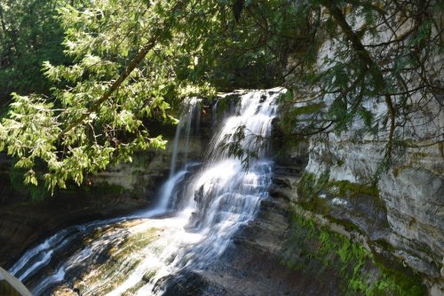 A serene waterfall cascading over rocky layers, surrounded by lush green trees and foliage.