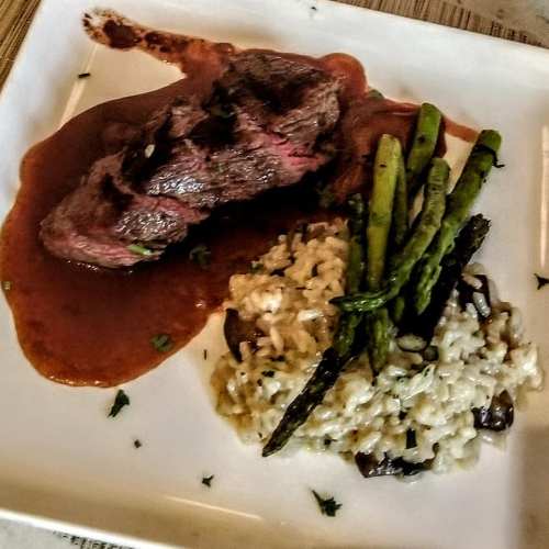 A plate featuring a steak with sauce, asparagus, and mushroom risotto, garnished with herbs.