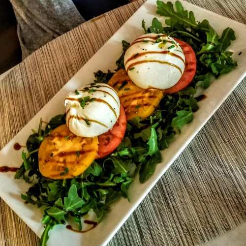 A fresh salad with arugula, sliced tomatoes, and two balls of mozzarella drizzled with balsamic glaze.