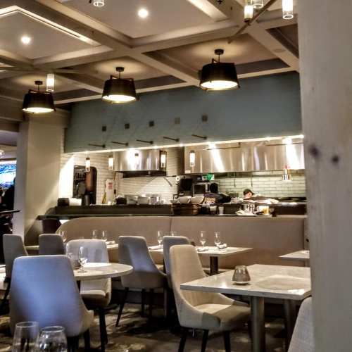 A modern restaurant interior featuring tables, chairs, and an open kitchen with chefs at work.