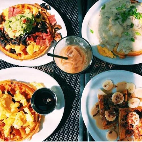 A table with four plates of waffles topped with various ingredients and a glass of iced coffee.