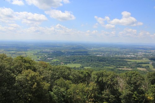 A panoramic view of lush green fields and hills under a blue sky with fluffy clouds.