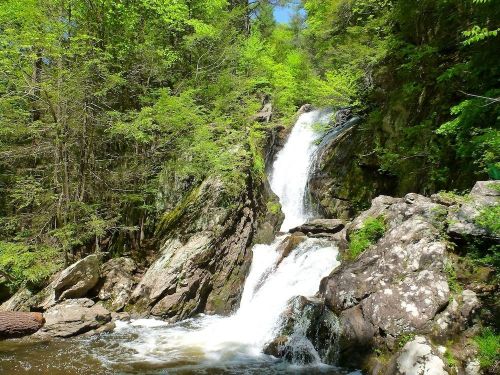 A serene waterfall cascading over rocky terrain, surrounded by lush green trees and bright blue sky.