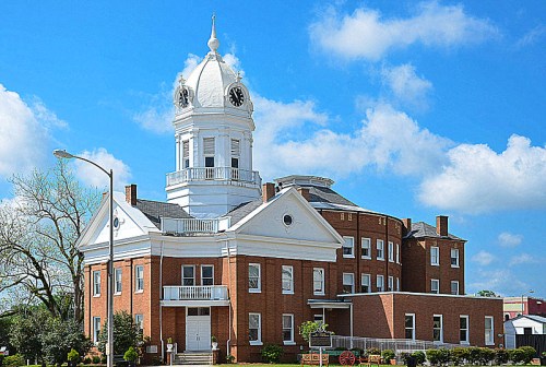 Historic brick building with a white clock tower, surrounded by blue skies and fluffy clouds.