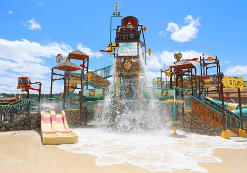 A vibrant water park with a large play structure, water slides, and splashing water under a bright blue sky.