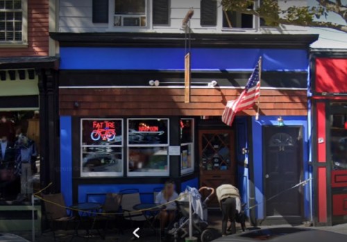 A colorful storefront with an American flag, featuring a bike shop sign and outdoor seating.