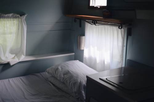 Cozy interior of a small room with a bed, window, and shelf, featuring soft lighting and a calming color palette.