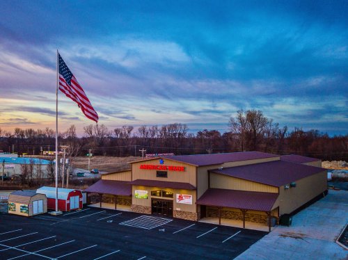 A large building with a flagpole displaying the American flag, set against a colorful sunset sky.