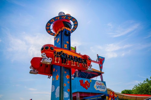 A colorful amusement park ride with a spaceship design, featuring excited riders against a bright blue sky.