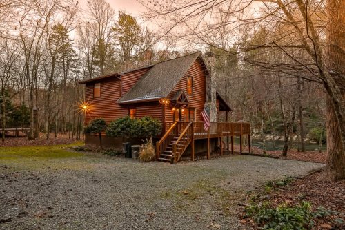 A cozy wooden cabin surrounded by trees, featuring a porch and an American flag, set in a serene, wooded area.