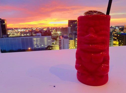 A vibrant sunset over a city skyline, with a red tiki mug in the foreground.