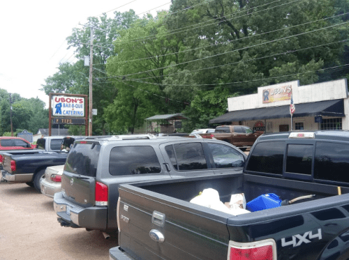 A row of parked trucks outside Ubon's Bar-B-Q restaurant, surrounded by trees and power lines.