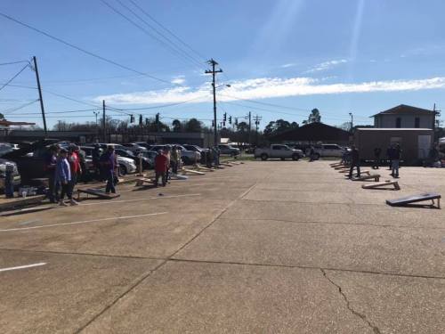 A sunny parking lot with people participating in an outdoor event, set up with equipment on the ground.