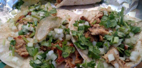 Three tacos filled with seasoned meat, chopped onions, and fresh cilantro, served on soft tortillas.