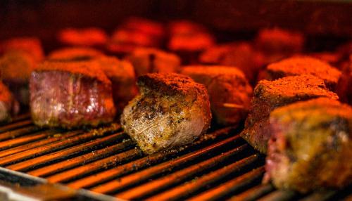 Grilled meat cubes with a smoky char, arranged on a grill with a warm, glowing background.