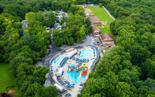 Aerial view of a water park surrounded by lush greenery, featuring pools, slides, and lounge chairs.