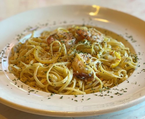 A plate of linguine pasta topped with shrimp, garnished with herbs and lemon slices.