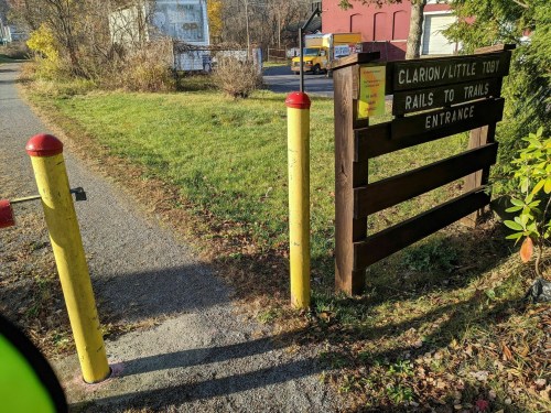 Entrance to the Clarion/Little Toby Rails to Trails, featuring a wooden sign and yellow posts along a gravel path.