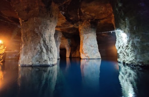 Underground cavern with large stone pillars and calm blue water, illuminated by soft lights.